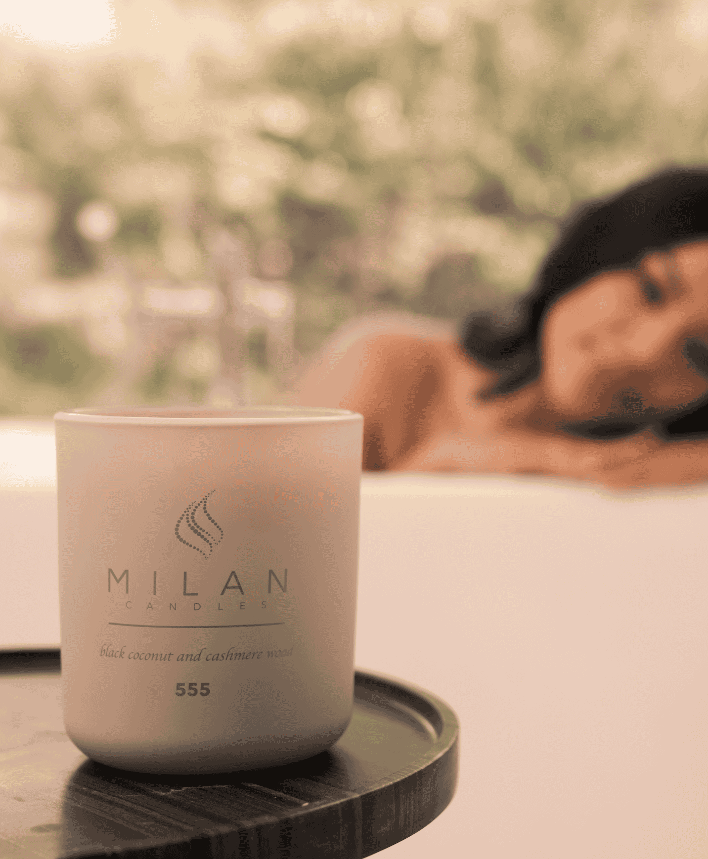 Candle with 'Milan Candles' branding on a table while woman is relaxing