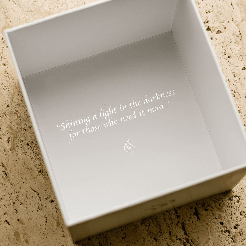 Milan Candle's box with engraved text on a textured surface that reads "Shining a light in the darkness for those who need it most".